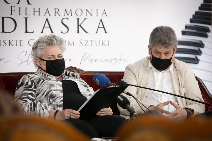 Profesor Bielecka siedzi na kanapie, z lewej strony, po prawej jest maestro Błaszczyk. Za nimi znajduje się ścianka opery, widać część napisu: "Opera i Filharmonia Podlaska" oraz fragment klawiatury fortepianu