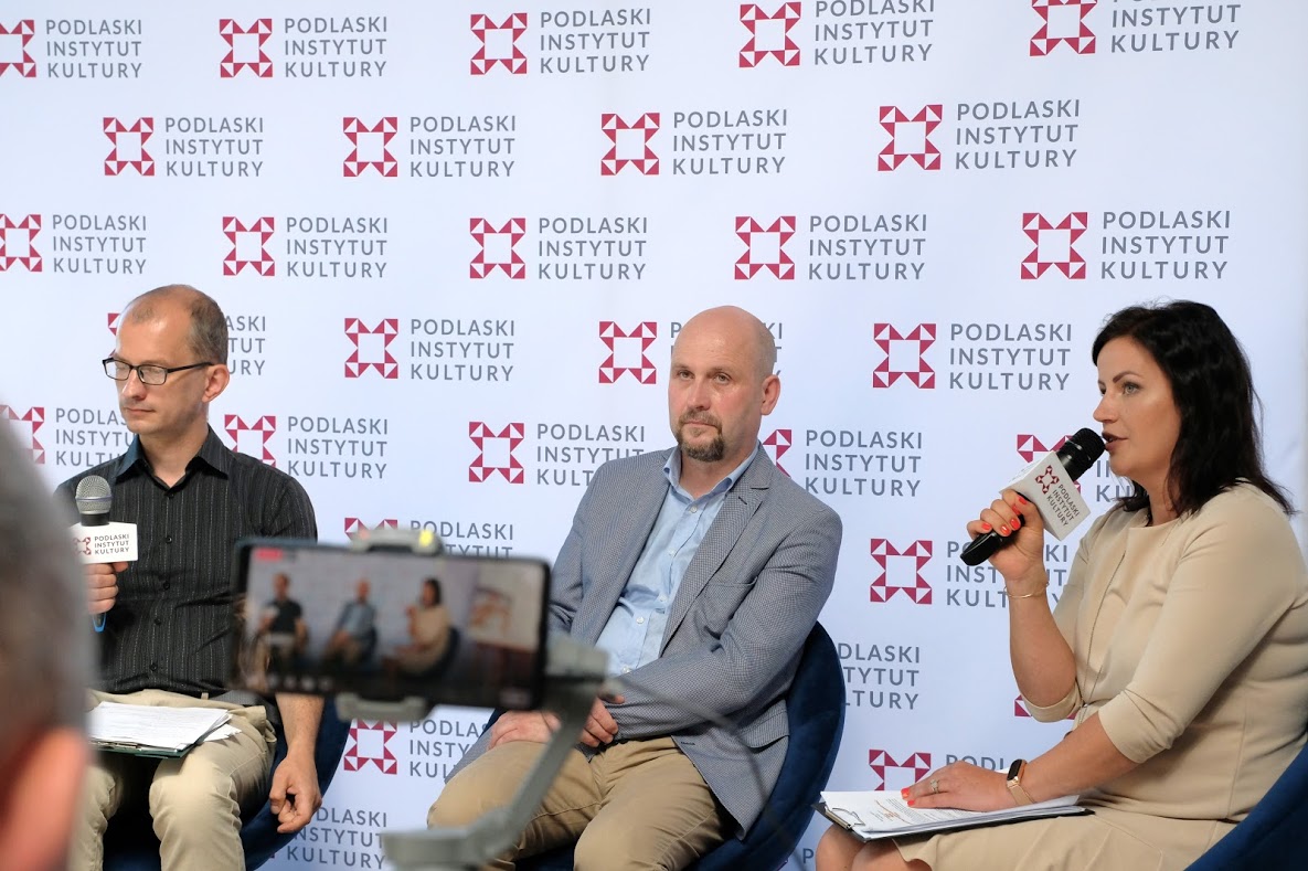 Trzy osoby siedzą na tle ścianki Podlaskiego Instytutu Kultury