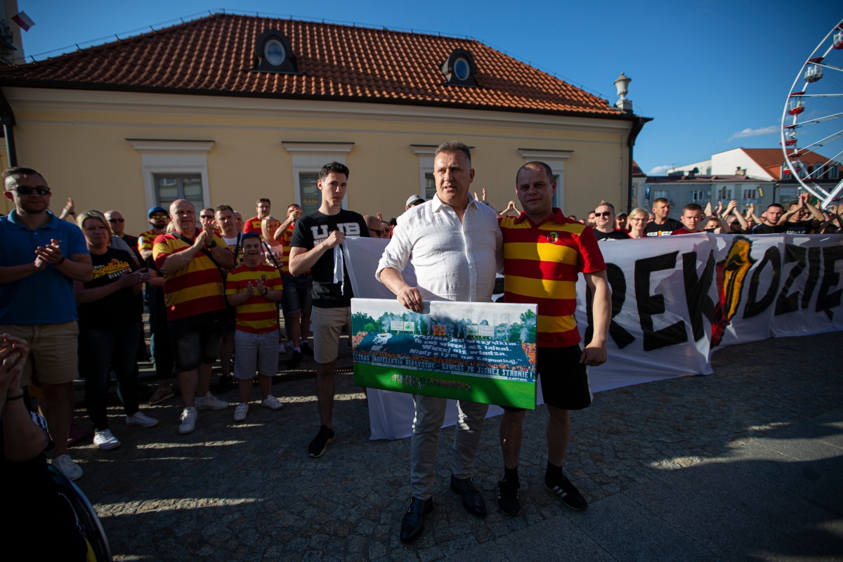 Na Rynku Kościuszki stoi były prezes Jagiellonii Cezary Kulesza., z lewej strony. Obok niego znajduje się fan drużyny. Za nimi stoi grupa kibiców żółto - czerwonych, część z nich trzyma transparent z napisem: Czarek, dzięki!