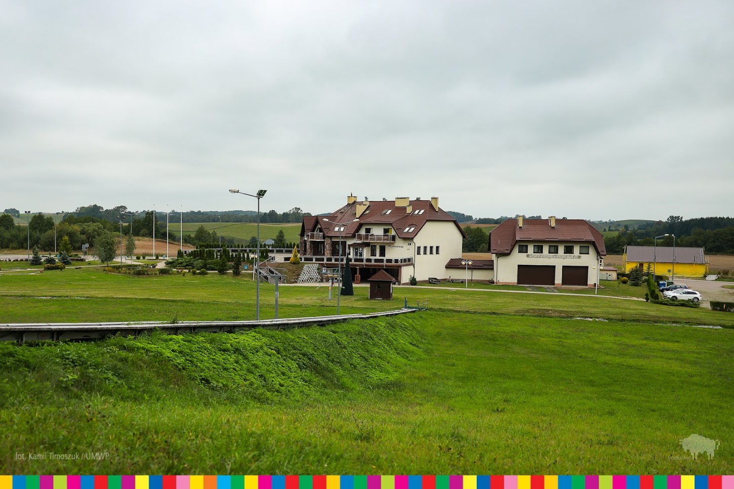 W oddali widać ośrodek Szelment. Na pierwszym planie jest trawa, dużo zieleń, dalej stoją budynki ośrodka