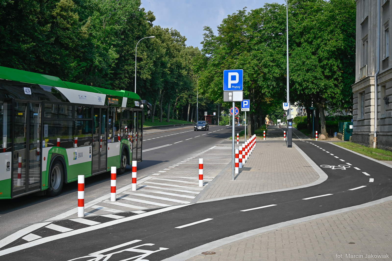 ścieżka rowerowa przy parku, ulicą jedzie autobus