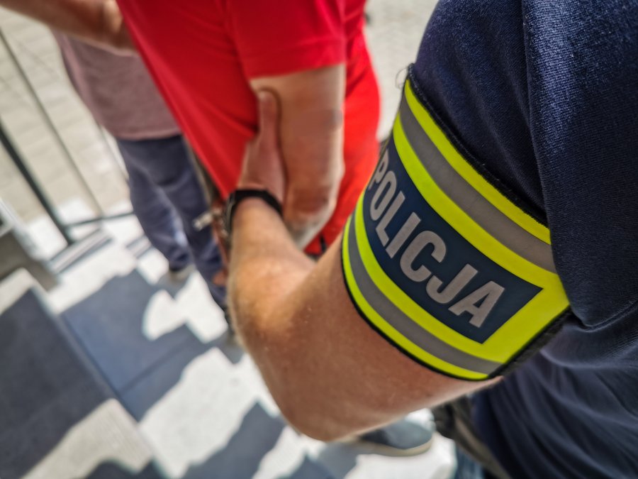 Policjant trzyma pod rękę skutego kajdankami mężczyznę