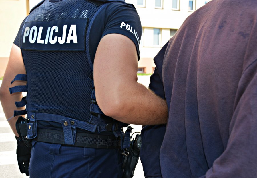 Policjant trzyma pod rękę aresztowanego mężczyznę