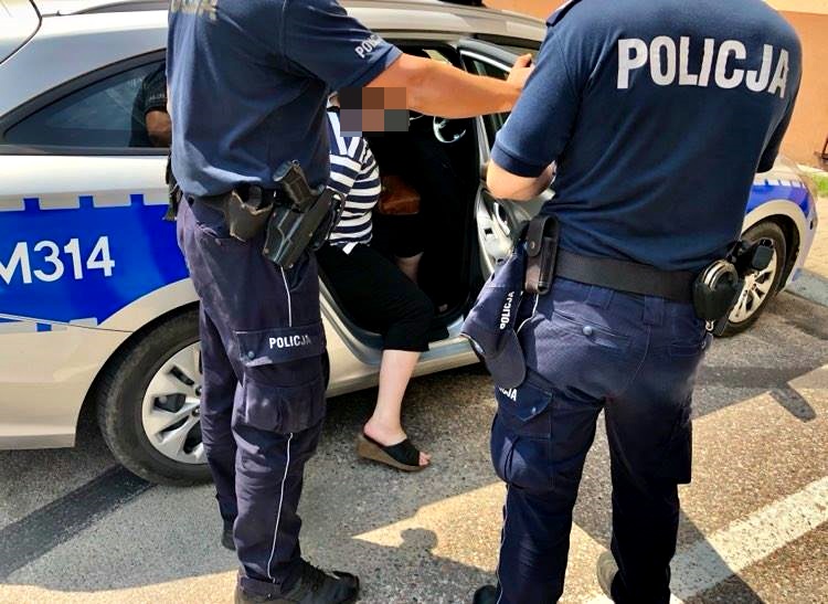 Dwaj policjanci wsadzają do radiowozu aresztowaną kobietę