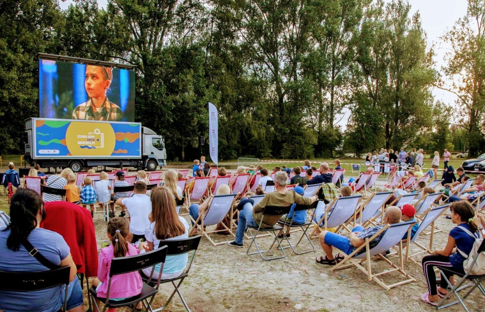 Kino plenerowe; ludzie siedzący na leżakach oglądają film na dużym ekranie
