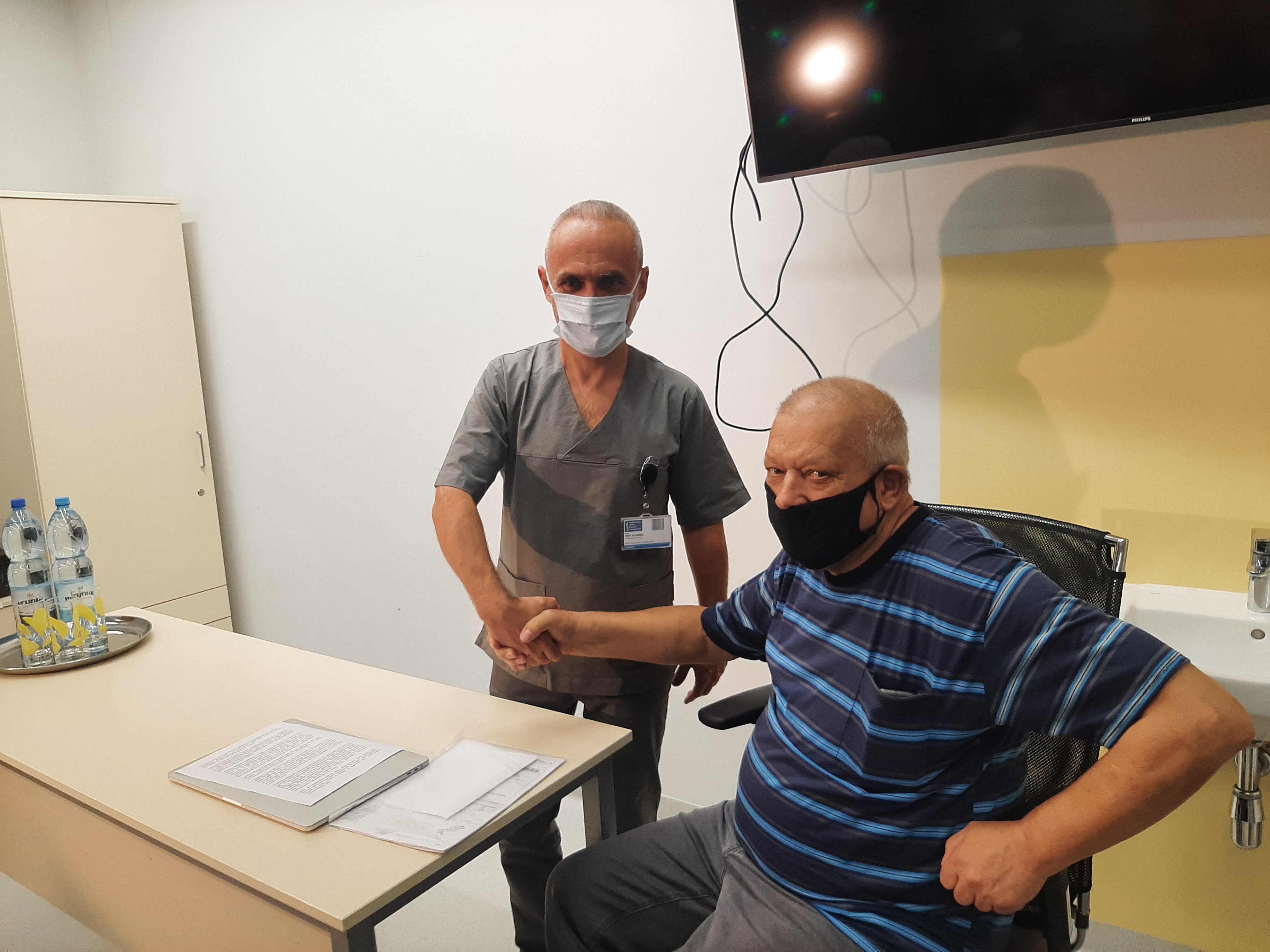 Lekarz stoi przy biurku obok niego na krześle siedzi pacjent. Mężczyźni podają sobie dłonie