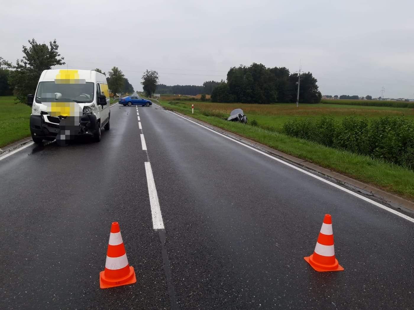 Na drodze ustawione są pachołki, w tle rozbity bus, opel w rowie i policyjny radiowóz