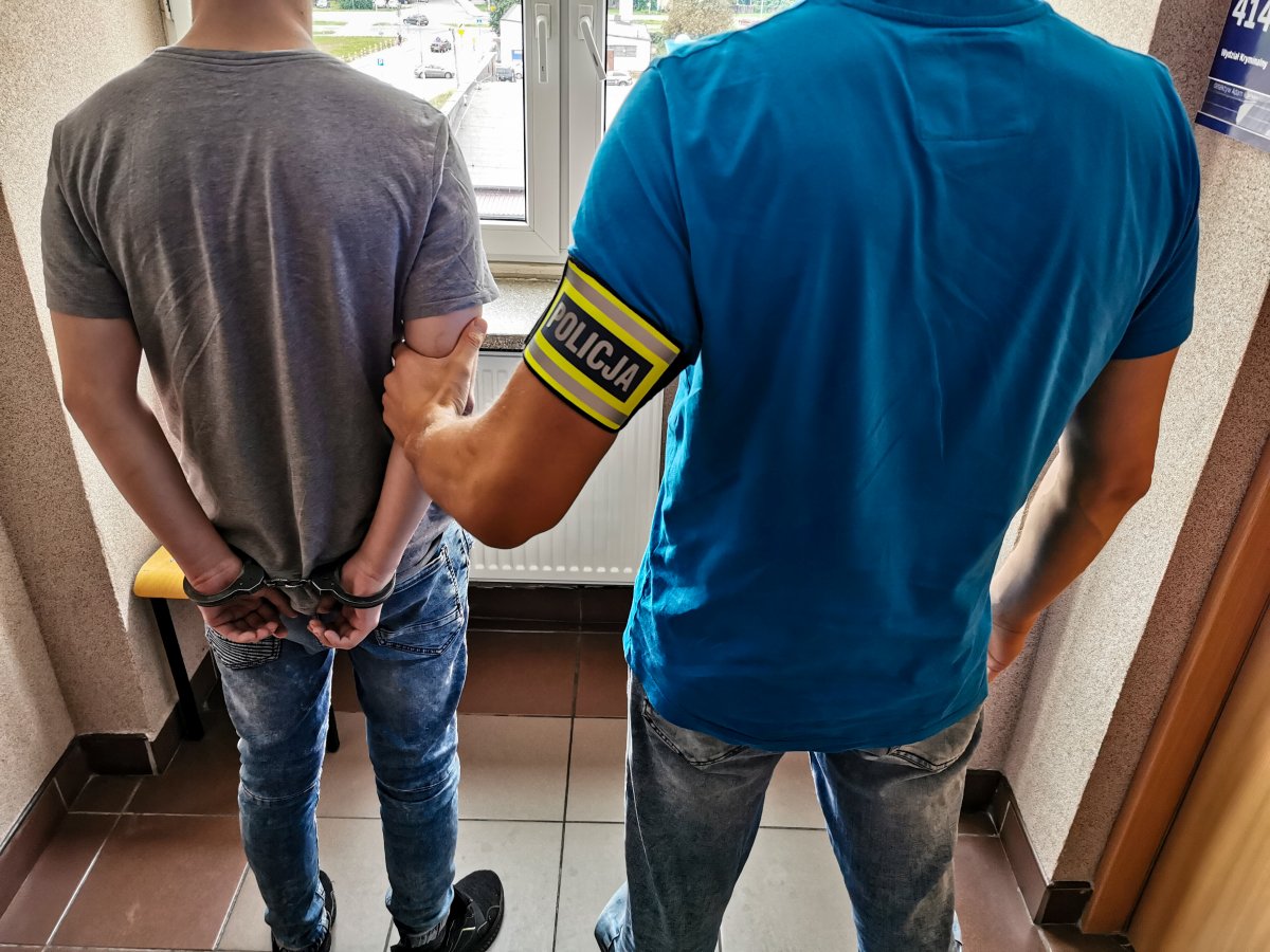 Policjant trzyma za rękę skutego kajdankami mężczyznę