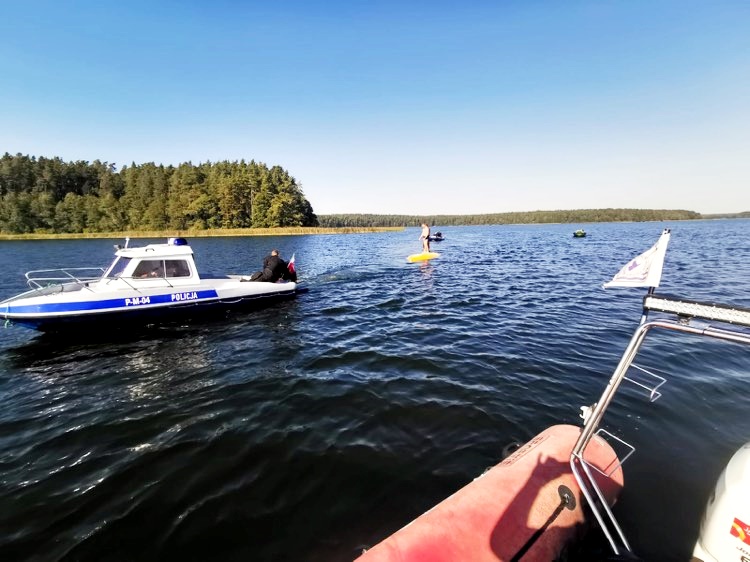 Na środku jeziora stoją dwie łodzie, trzecia łódź jest wywrócona