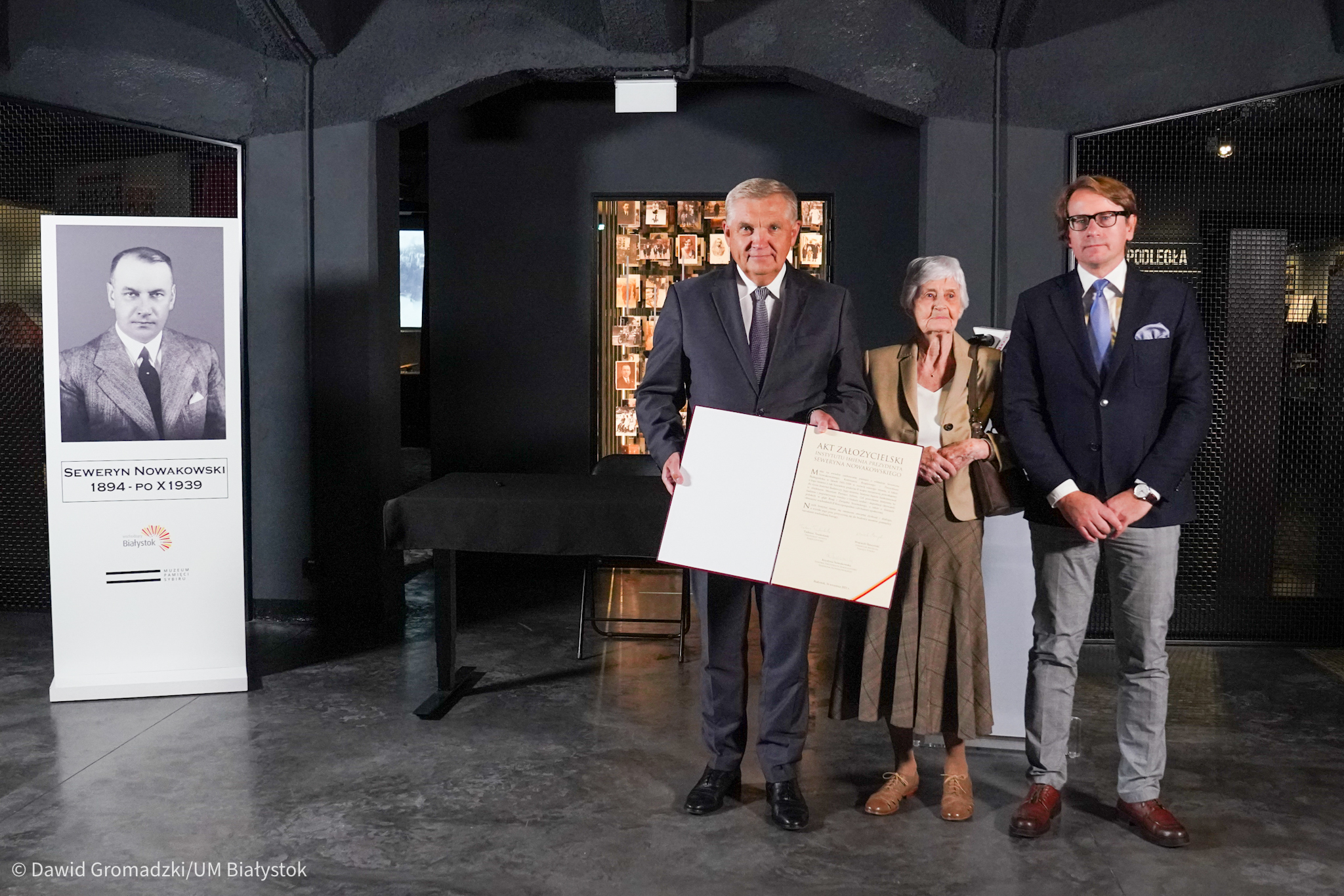 Z lewej strony stoi stand z wizerunkiem prezydenta Białegostoku Seweryna Nowakowskiego, z prawej stoi prezydent Białegostoku, Krystyna Nowakowska oraz dyrektor Muzeum Pamięci Sybiru.Prezydent Białegostoku trzyma w rękach akt założycielski instytutu badawczego
