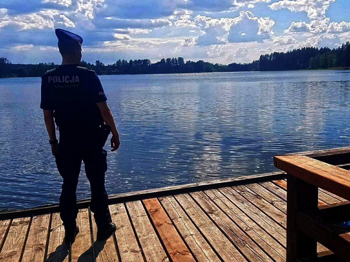 Policjant w granatowym mundurze stoi na moście, patrzy przed siebie, na wodę