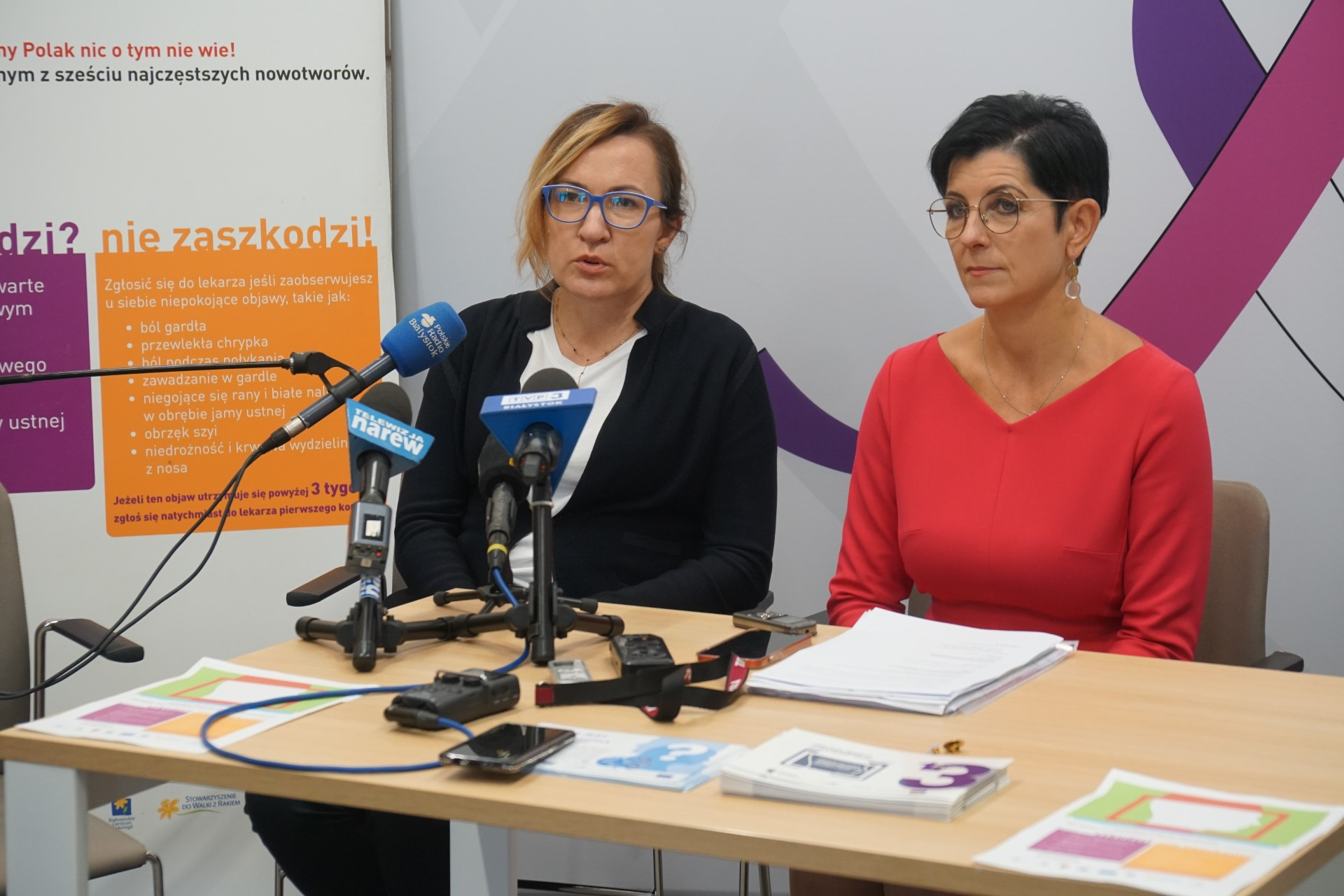 Przy stole siedzą dwie kobiety. Mówią do mikrofonów, które stoją na stole