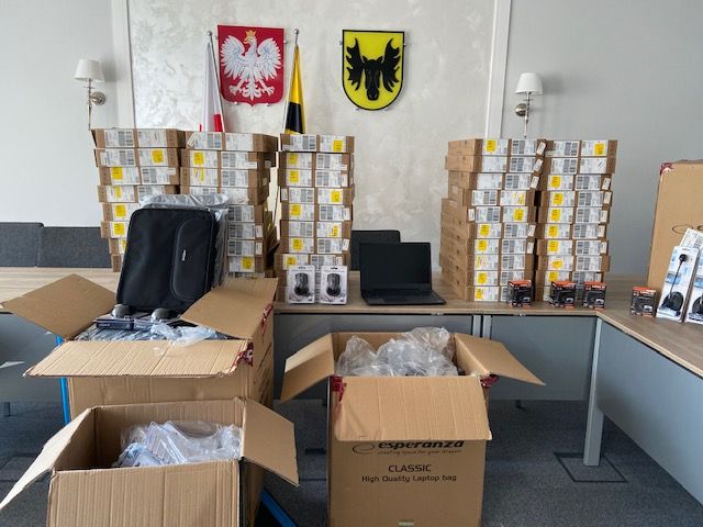Pomieszczenie urzędu. Na stole leżą i podłodze stoją kartony wypełnione sprzętem komputerowym