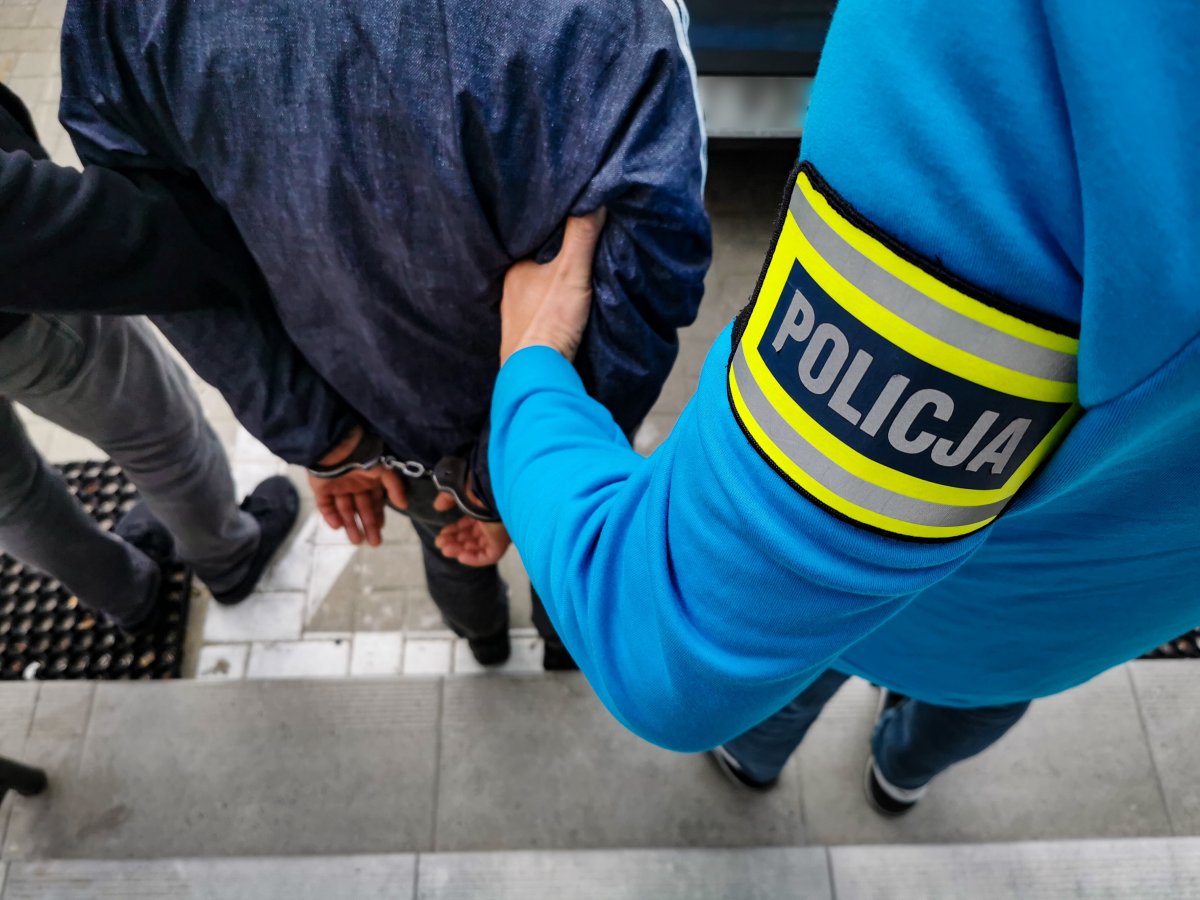 Dwaj policjanci trzymają za ramiona skutego kajdankami mężczyznę