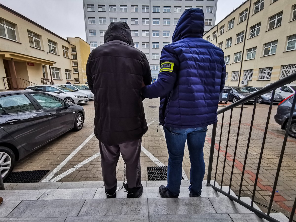 Policjant trzyma za ramię skutego kajdankami mężczyznę