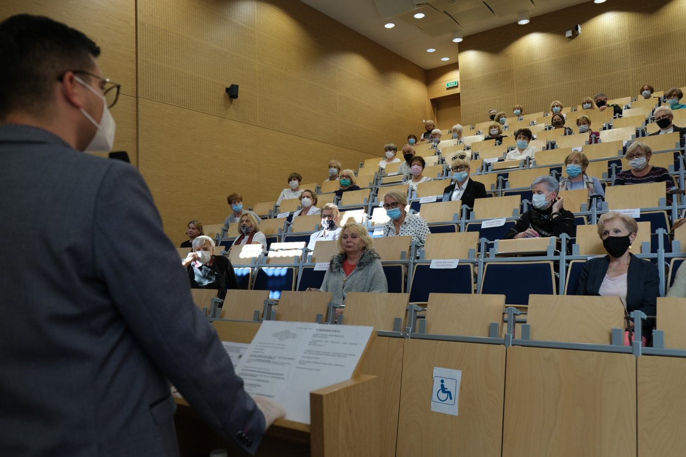 Uczelniana aula. Na krzesłach siedzą studenci-seniorzy