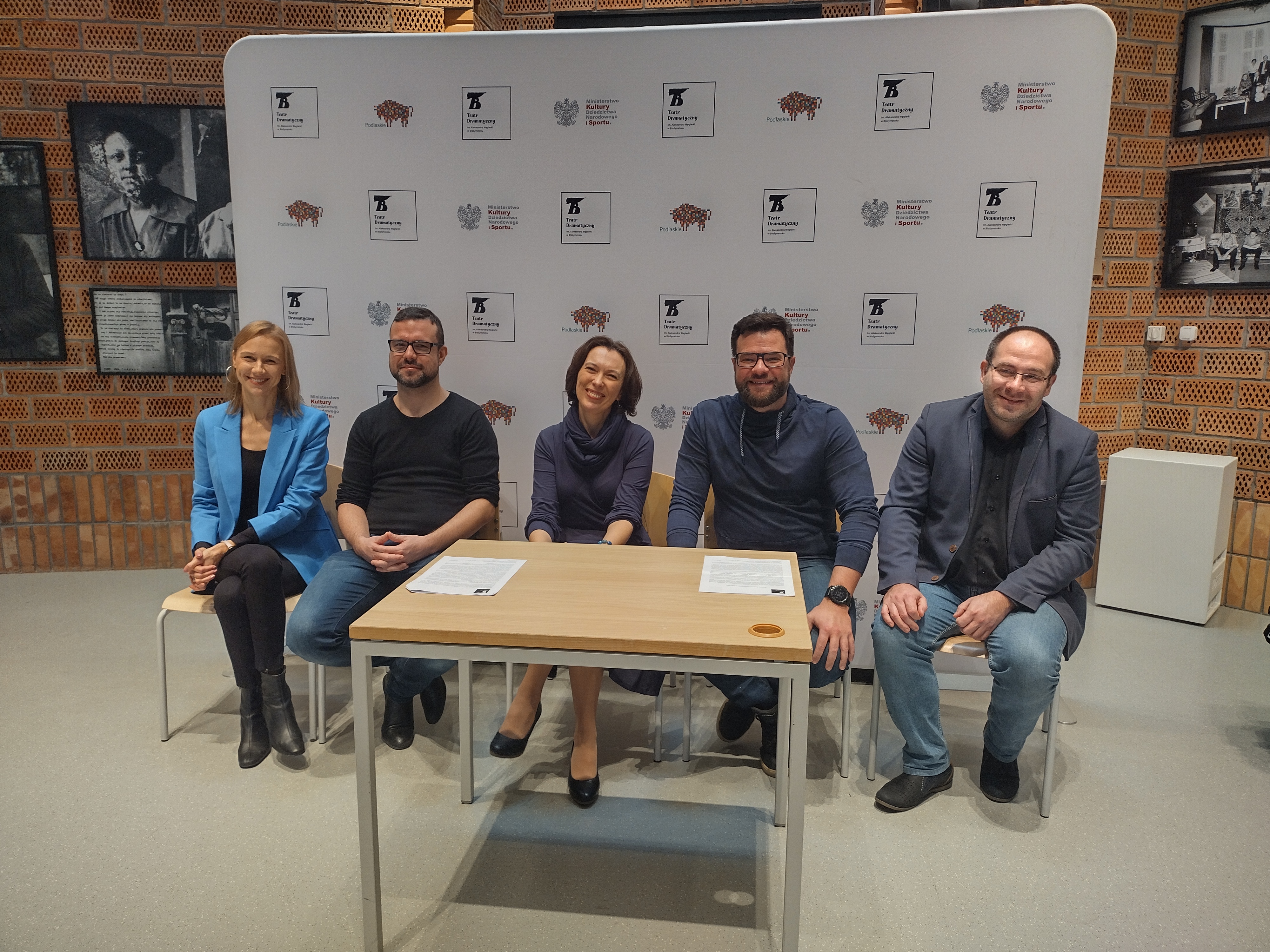 NA tle ścianki Teatru Dramatycznego siedzi pięć osób, przed nimi stoi stolik