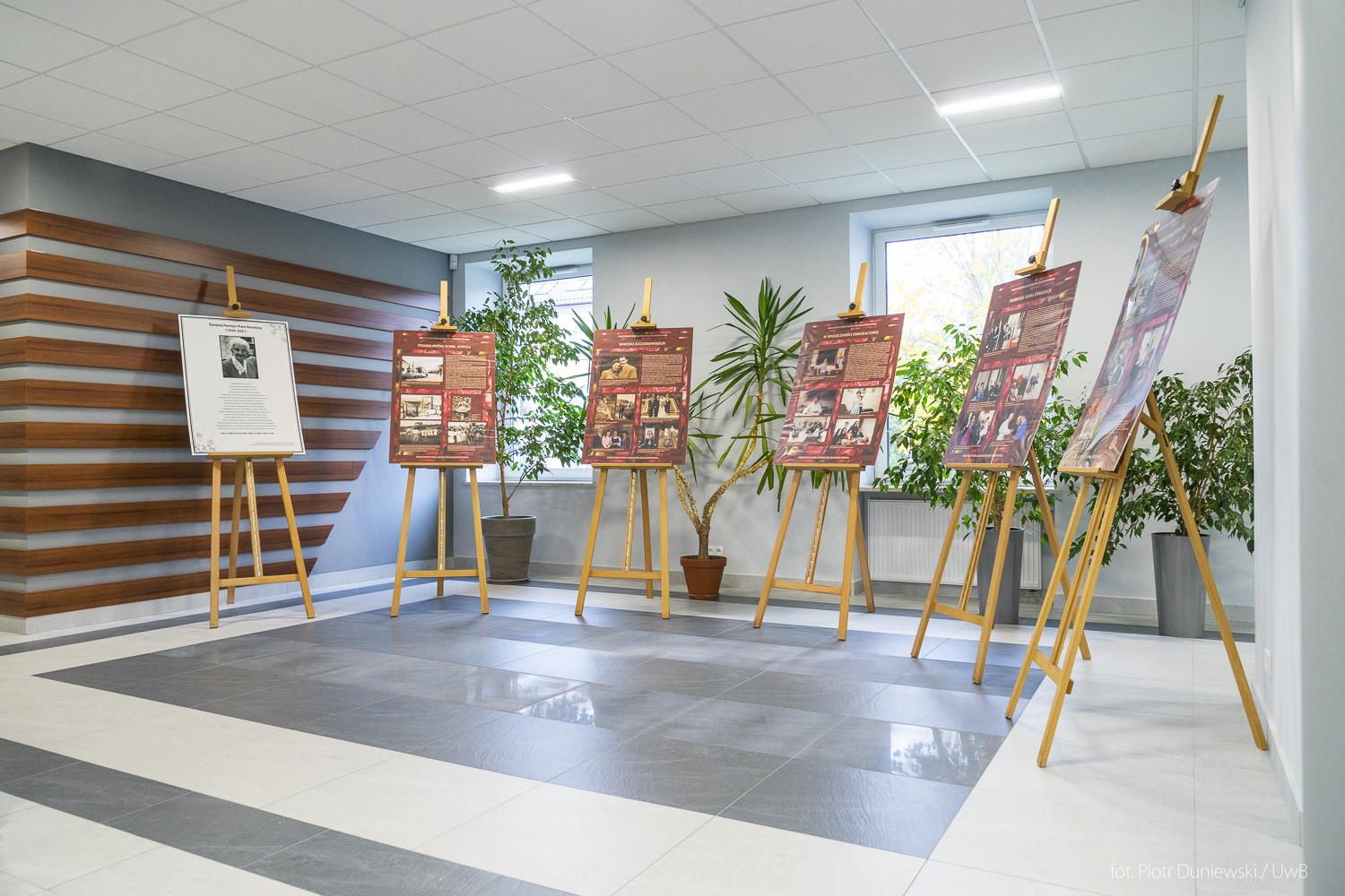 W korytarzu stoją sztalugi wypełnione fotosami