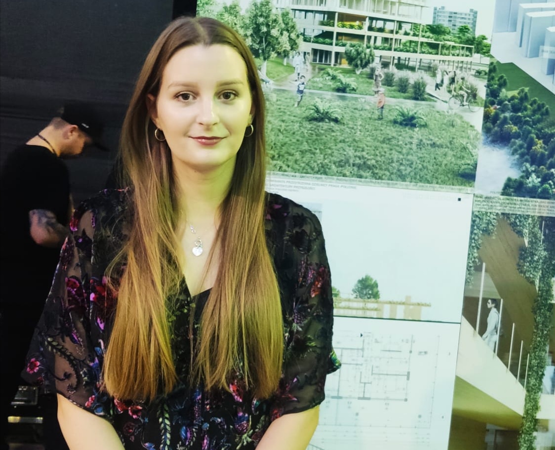 Dziewczyna z długimi ropuszczonymi włosami stoi na tle swego projektu architektonicznego