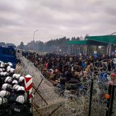 Kordon policji w białych kaskach stoi przed drutem kolczastym, który rozciągnięty jest na granicy