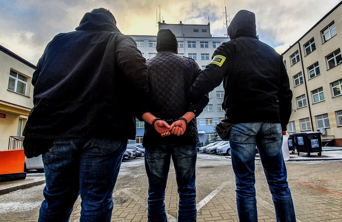 Dwaj policjanci trzymają skutego kajdankami mężczyznę