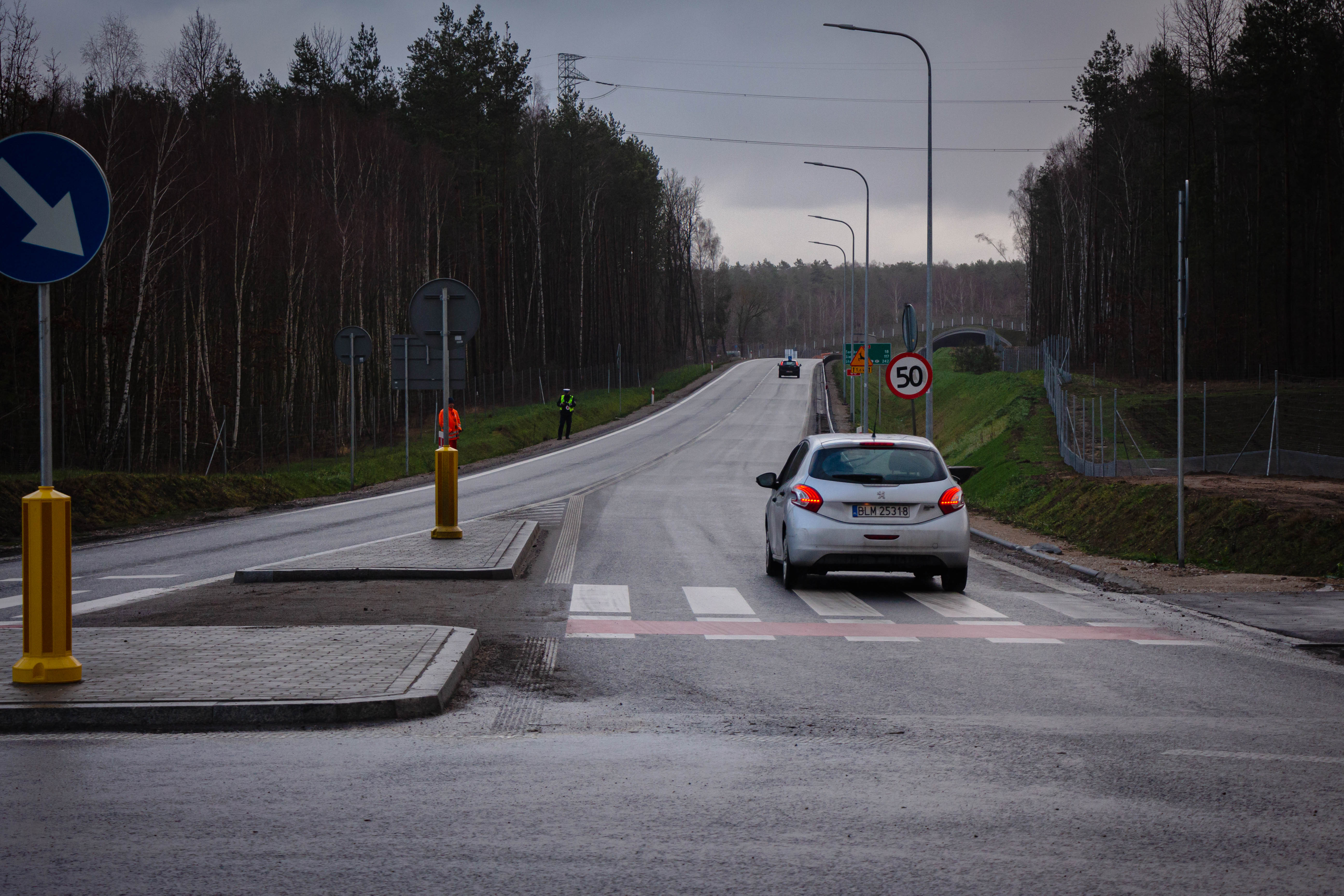 Droga poza terenem zabudowanym, po której jedzie jasny samochód. Auto widoczne jest od tyłu