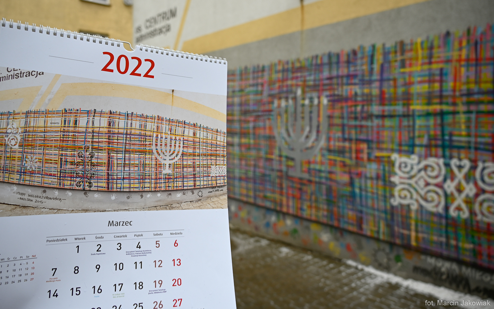 Z prawej strony jest mural utkany wielokulturowością. Malowidło przedstawia tkaninę utkaną z różnokolorowych nitek, w którą wplecione są białe elementy symbolizujące różne religie. Z lewej strony jest kalendarz ścienny, otwarty na stronie, na której znajduje się zdjęcie tego samego muralu