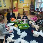 mężczyzna tworzy szmacianą lalkę, obok siedzą dzieci