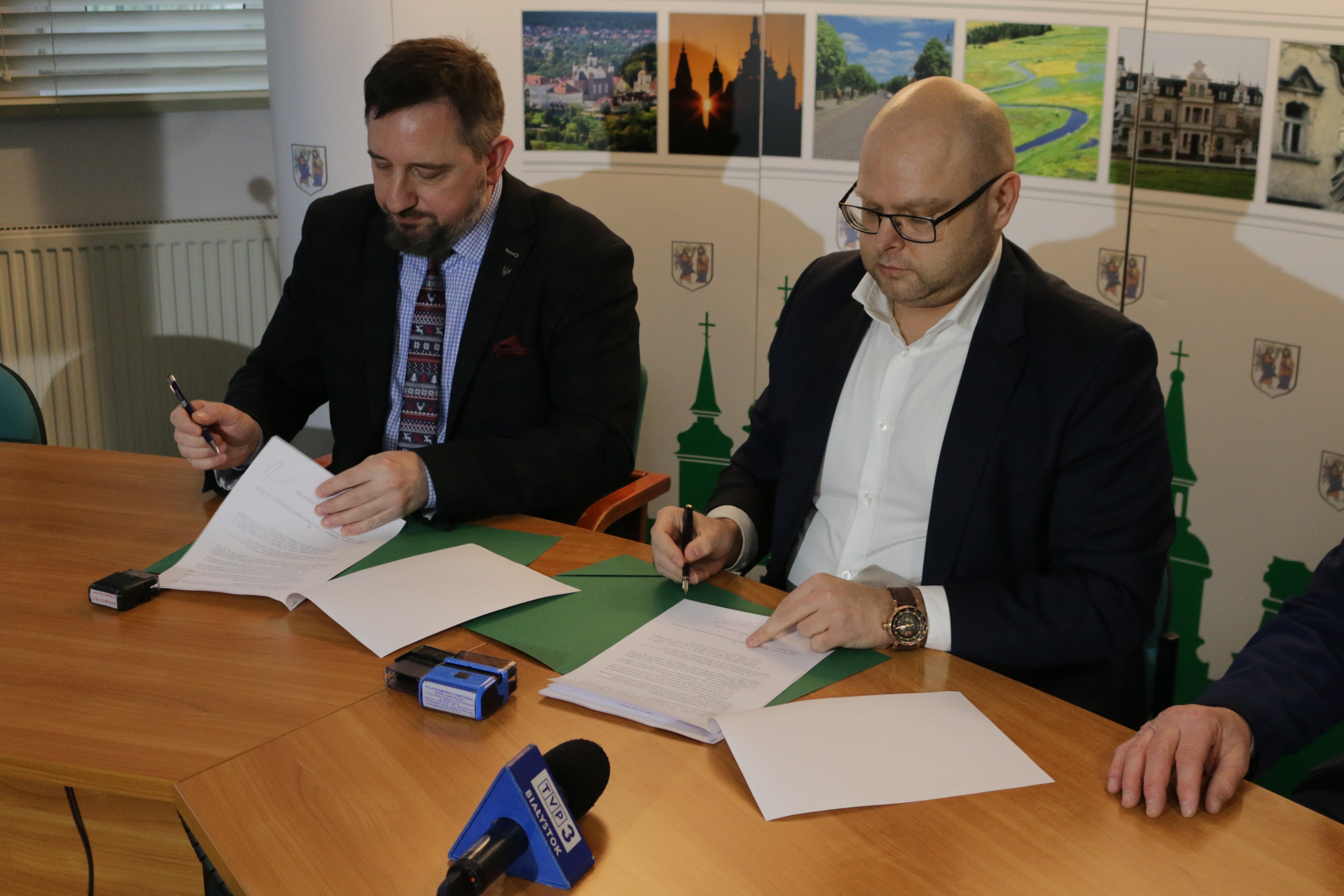 Dwóch mężczyzn siedzi przy jasnobrązowym stole i podpisują dokumenty