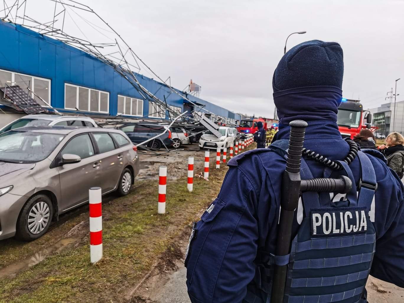 Policjant stoi przy budynku, z którego wystaje zerwana z dachu konstrukcja instalacji solarnej