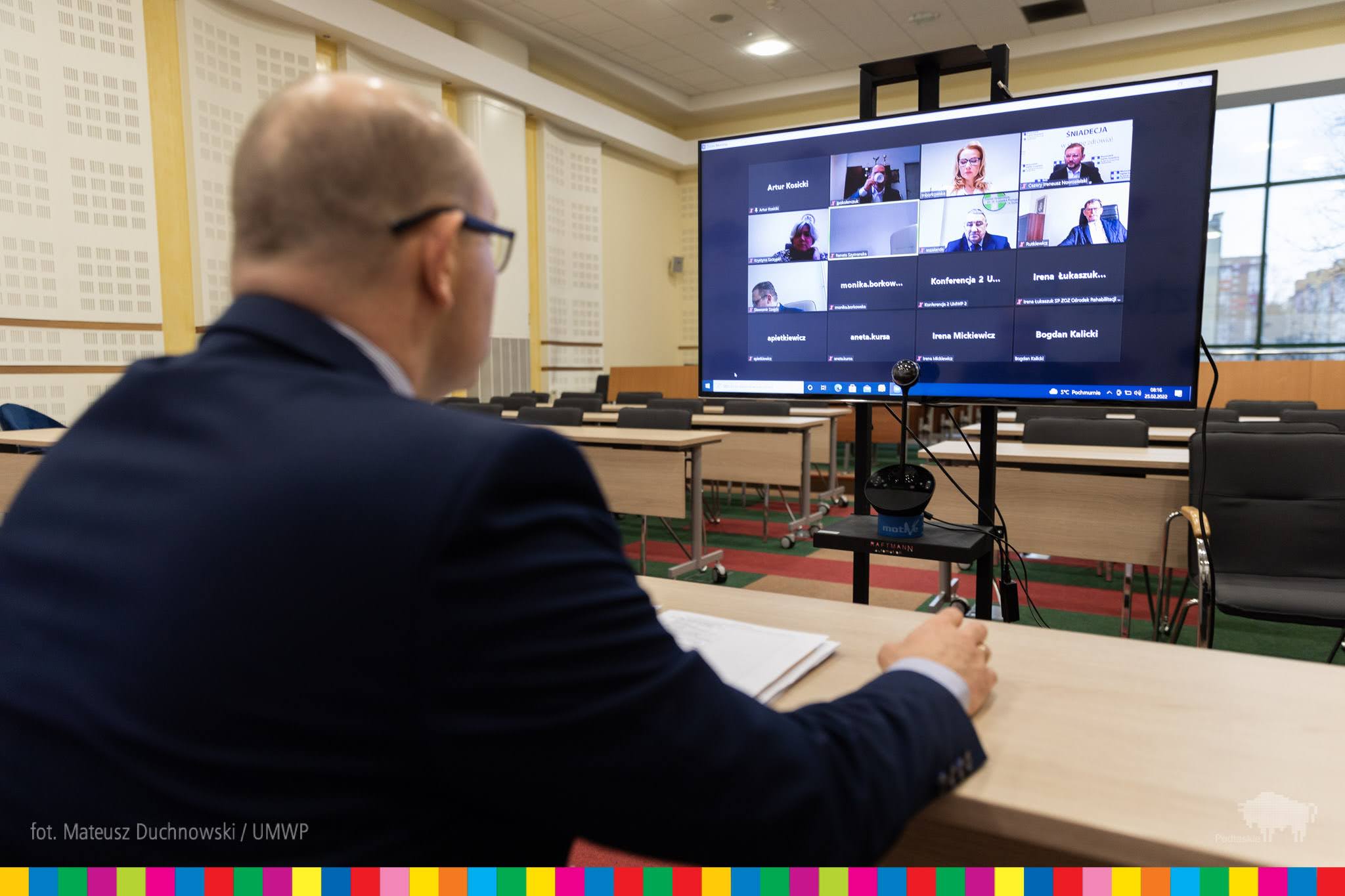 Mężczyzna siedzi przy biurku w tle telebim