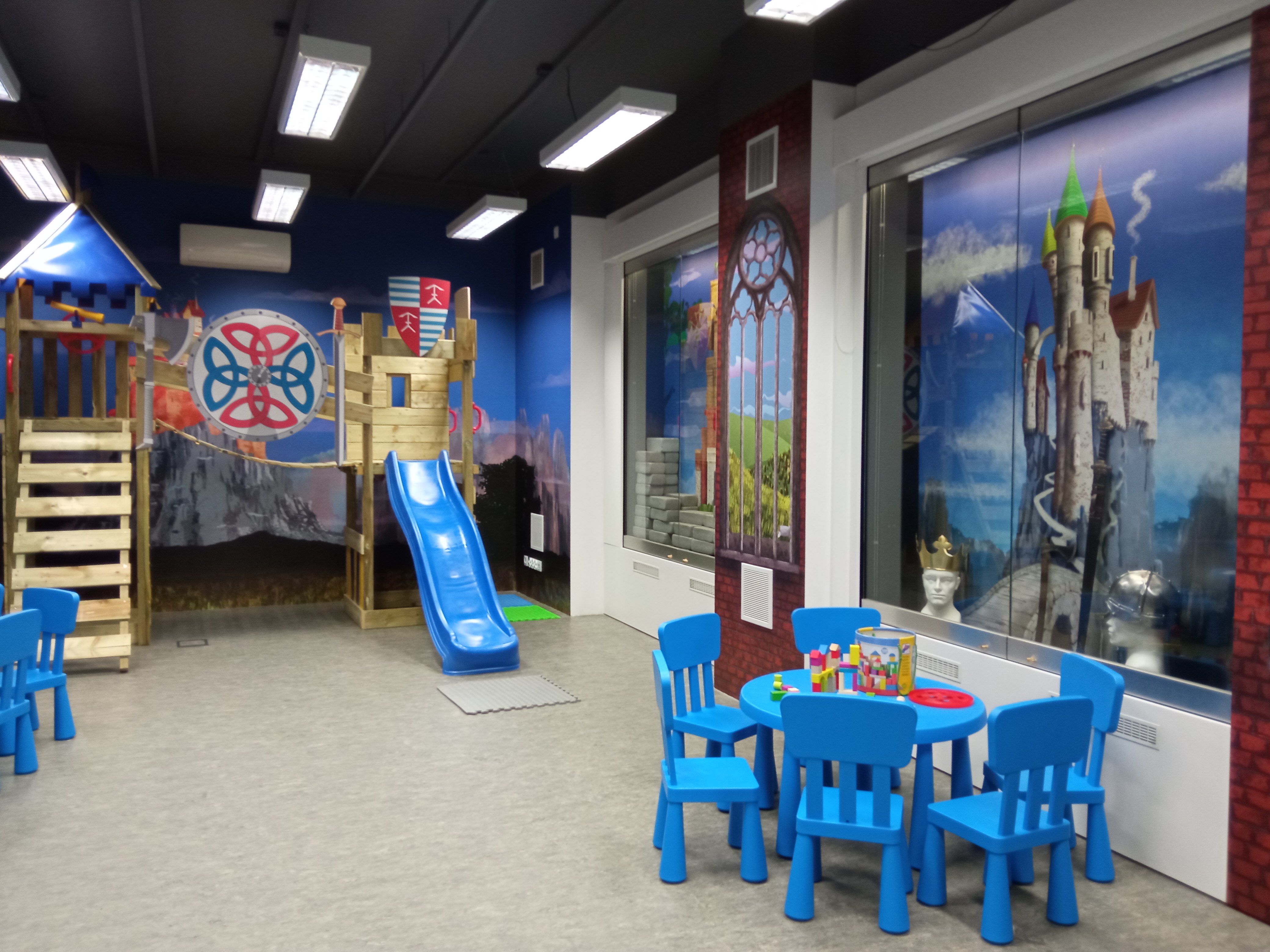 Centrum Edukacji dla najmłodszych, zainsccenizowany gród średniowieczny, krzesłka i stolik dla ddzieci, na ścianach namalowane zamki, okna