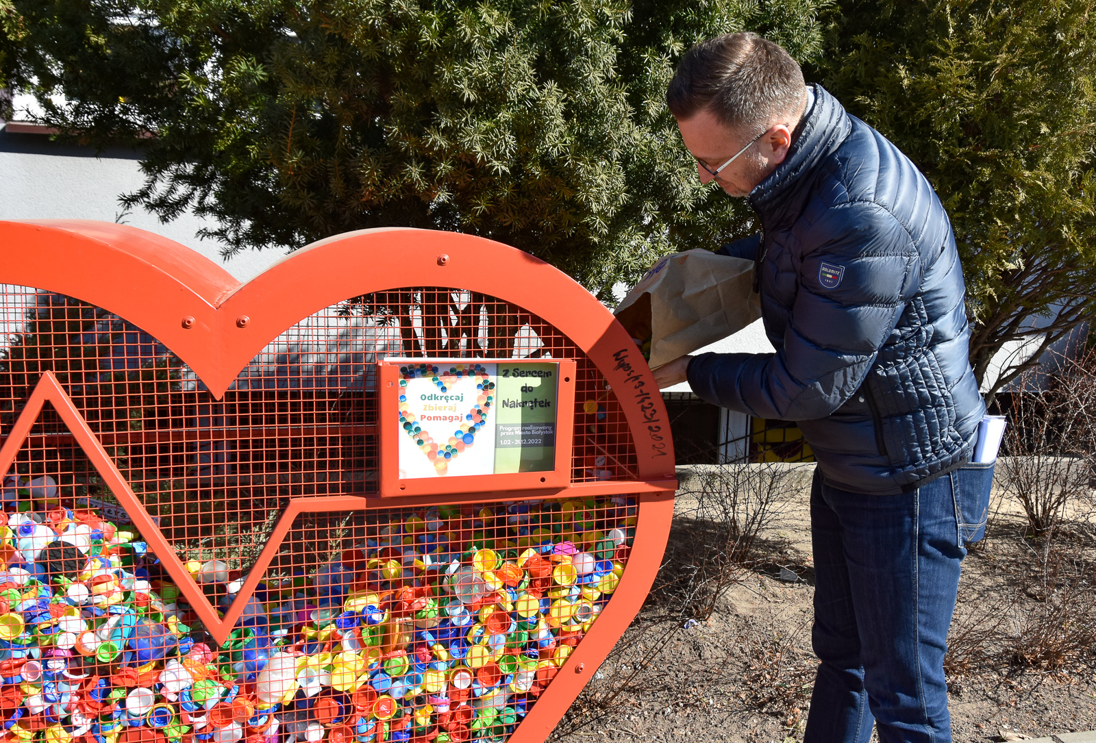 Mężczyzna wsypuje nakrętki z torby do metalowe kosza w kształcie serca