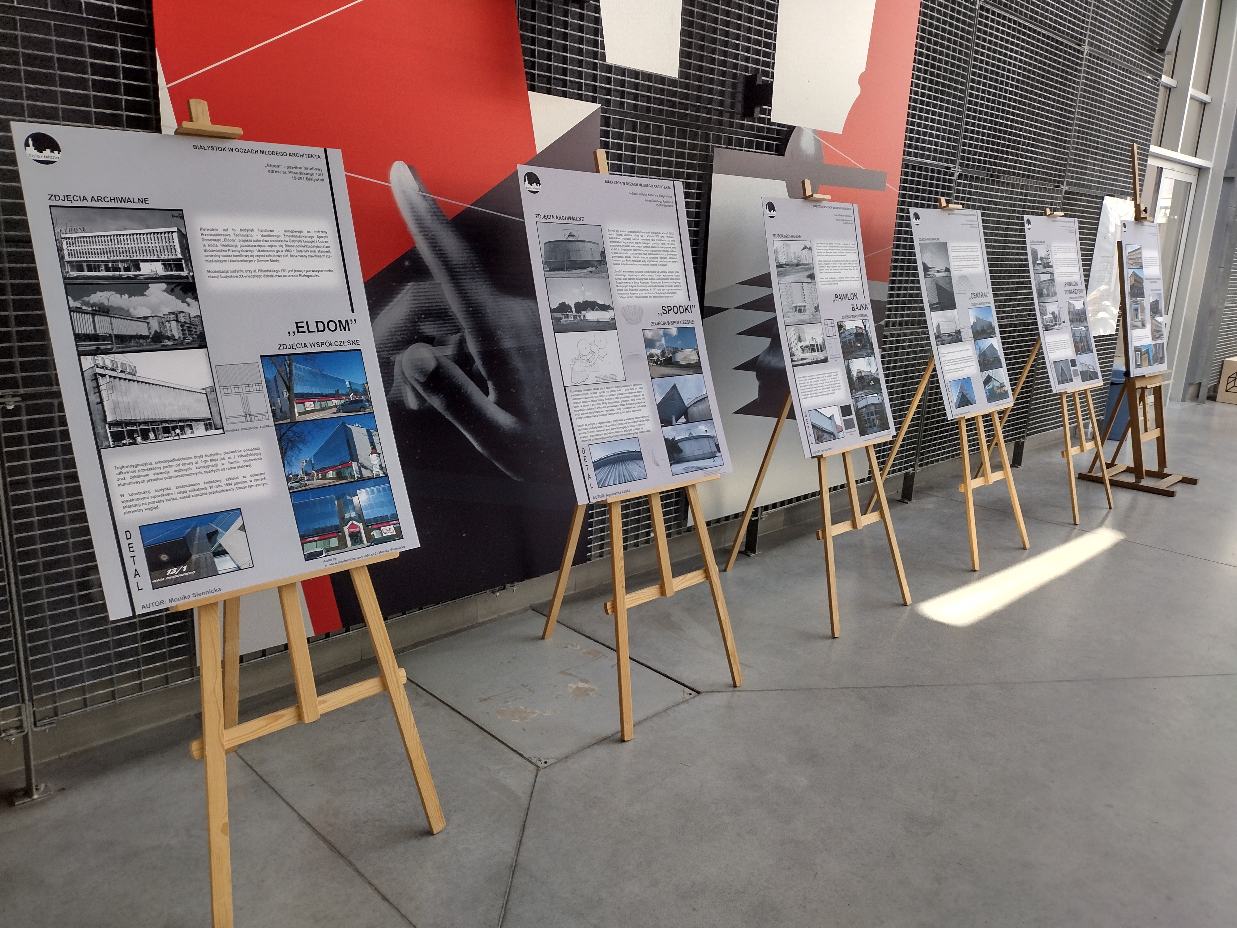 Hala w stylu industrialnym. Pod ścianą, z lewej strony stoją drewniane sztalugi z planszami na temat architektury modernistycznej w Białymstoku