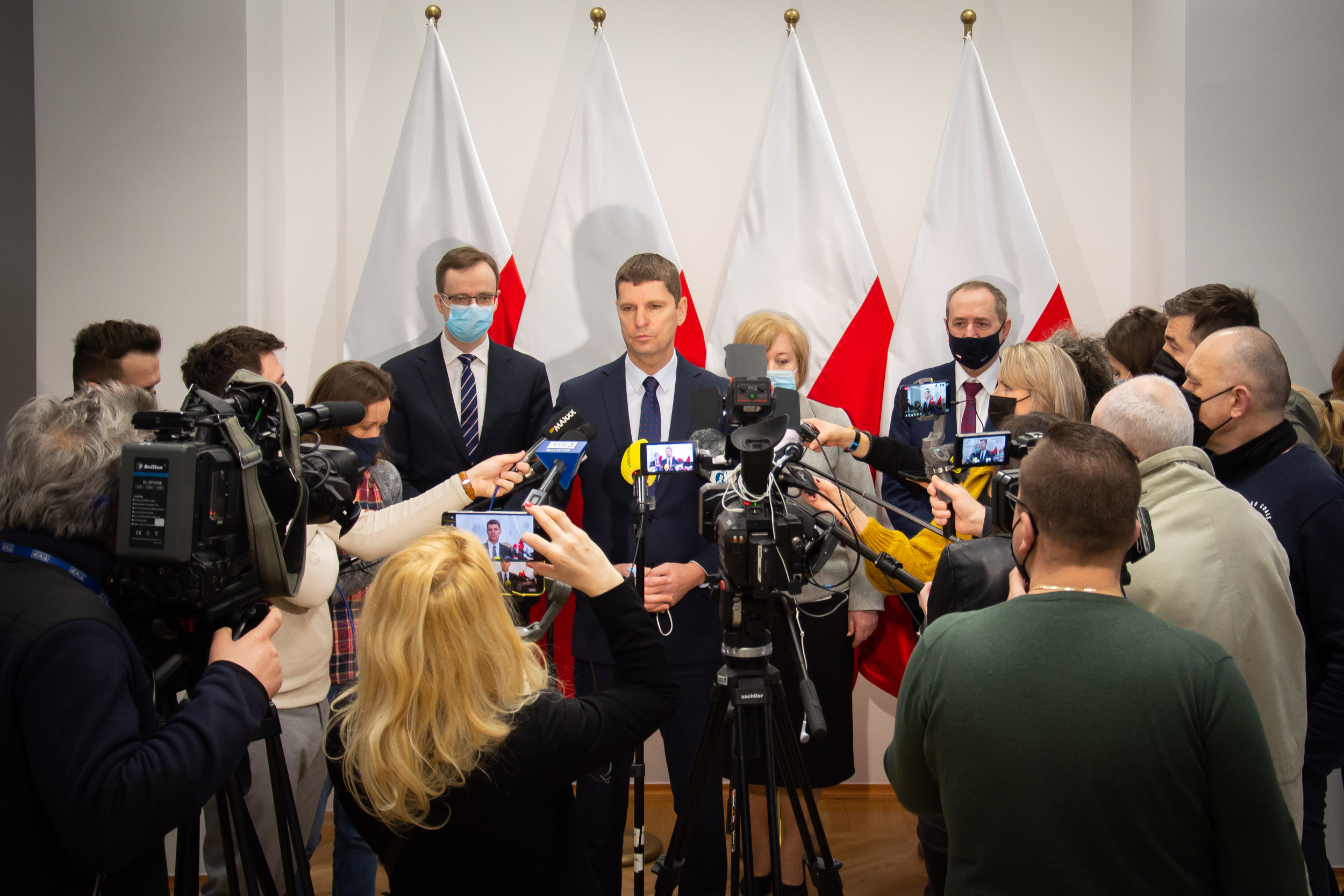 Ludzie stoją rzed mikrofonami na konferencji rasowej. Przed nimi stoją dziennikarze