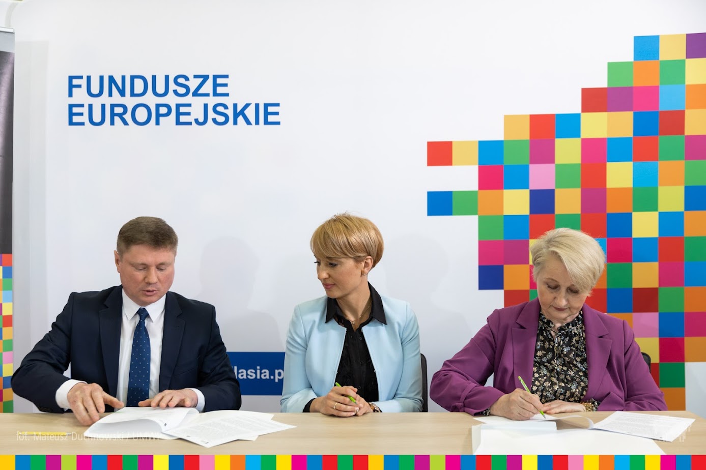 Trzy osoby przy stole podpisują papiery