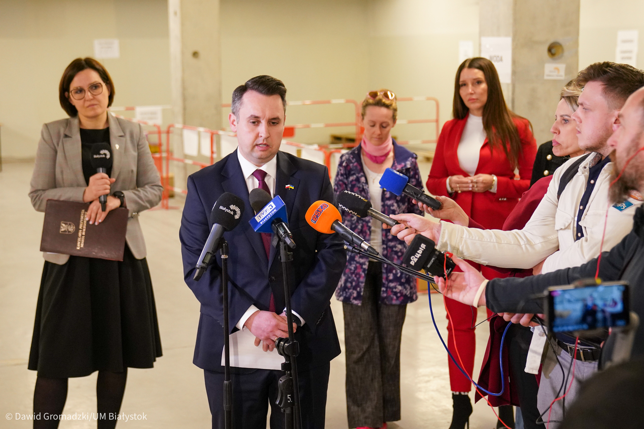 Konferencja prasowa, mężczyzna mówi do mikrofonów dziennikarzy