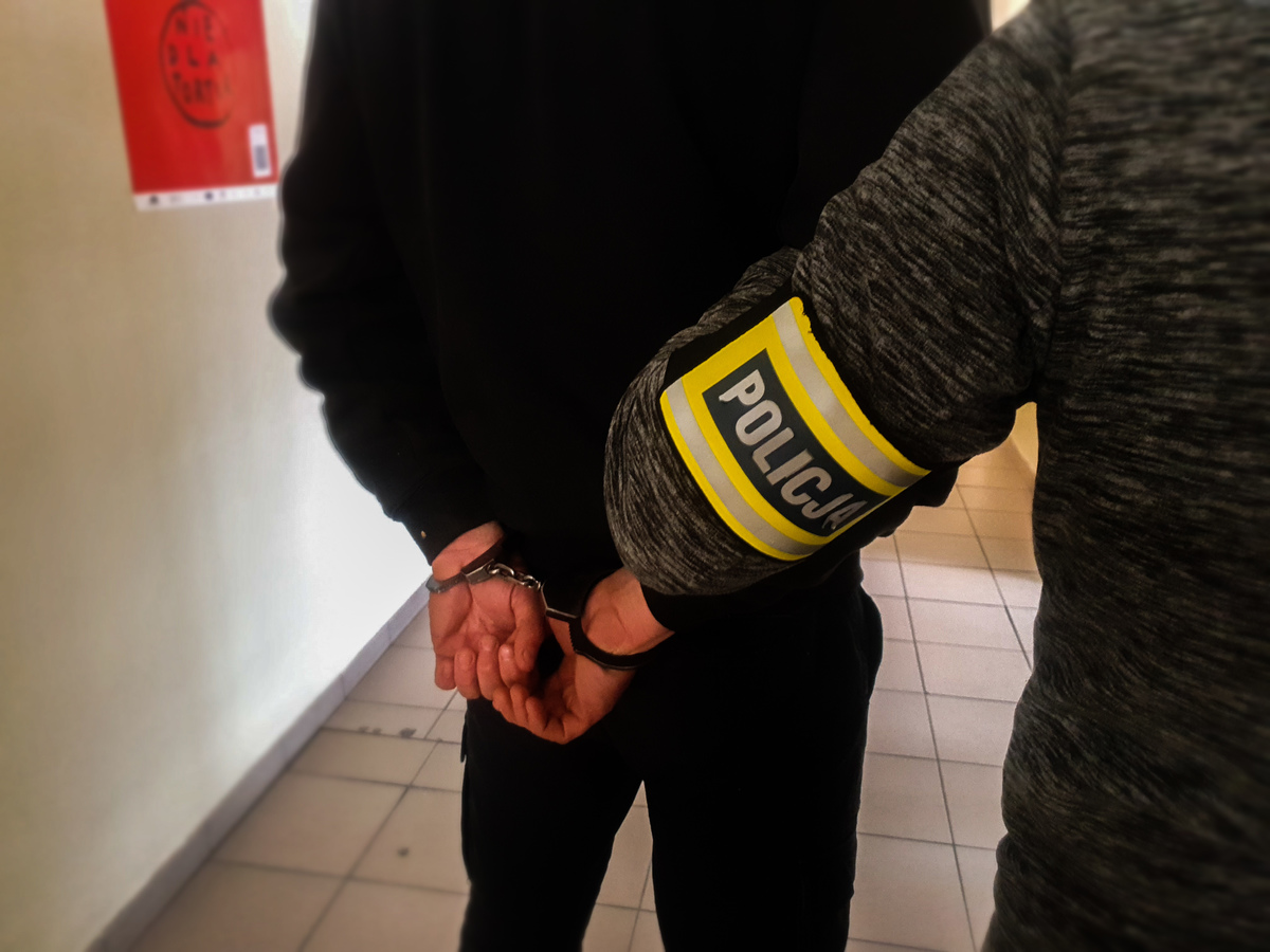 Policjant trzyma skutego kajdankami mężczyznę