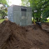 Na ziemi stoi budynek toalety, wokół trwają prace