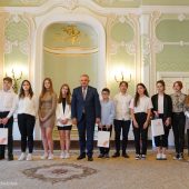 Na scenie stoi mężczyzna i nagrodzeni uczniowie