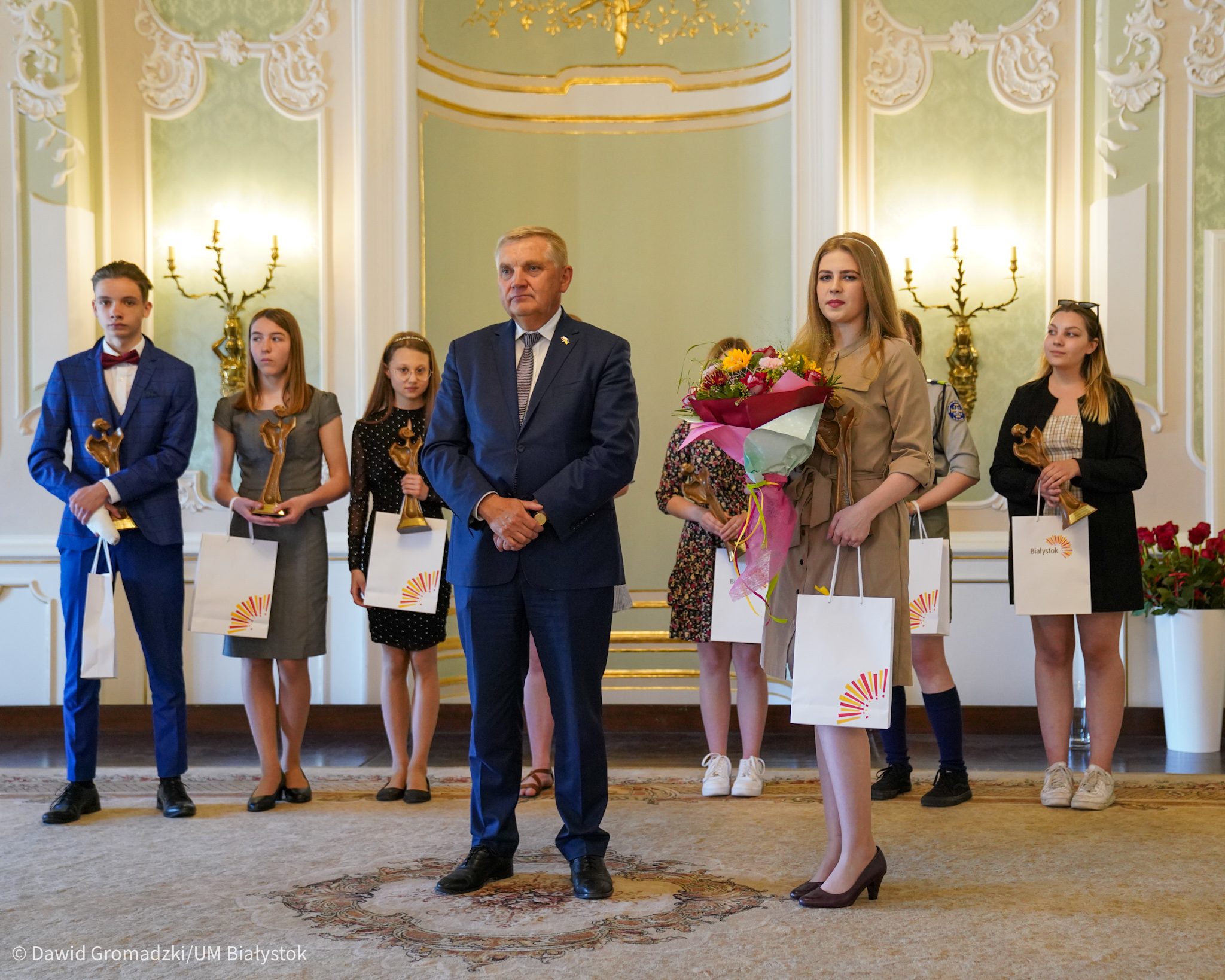 Na scenie stoi mężczyzna i nagrodzeni uczniowie