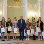 Na scenie stoi mężczyzna i nagrodzeni uczniowie