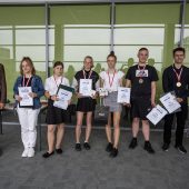 Grupa nagrodzonych uczniów stoi z dyplomami i medalami, obok stoi mężczyzna