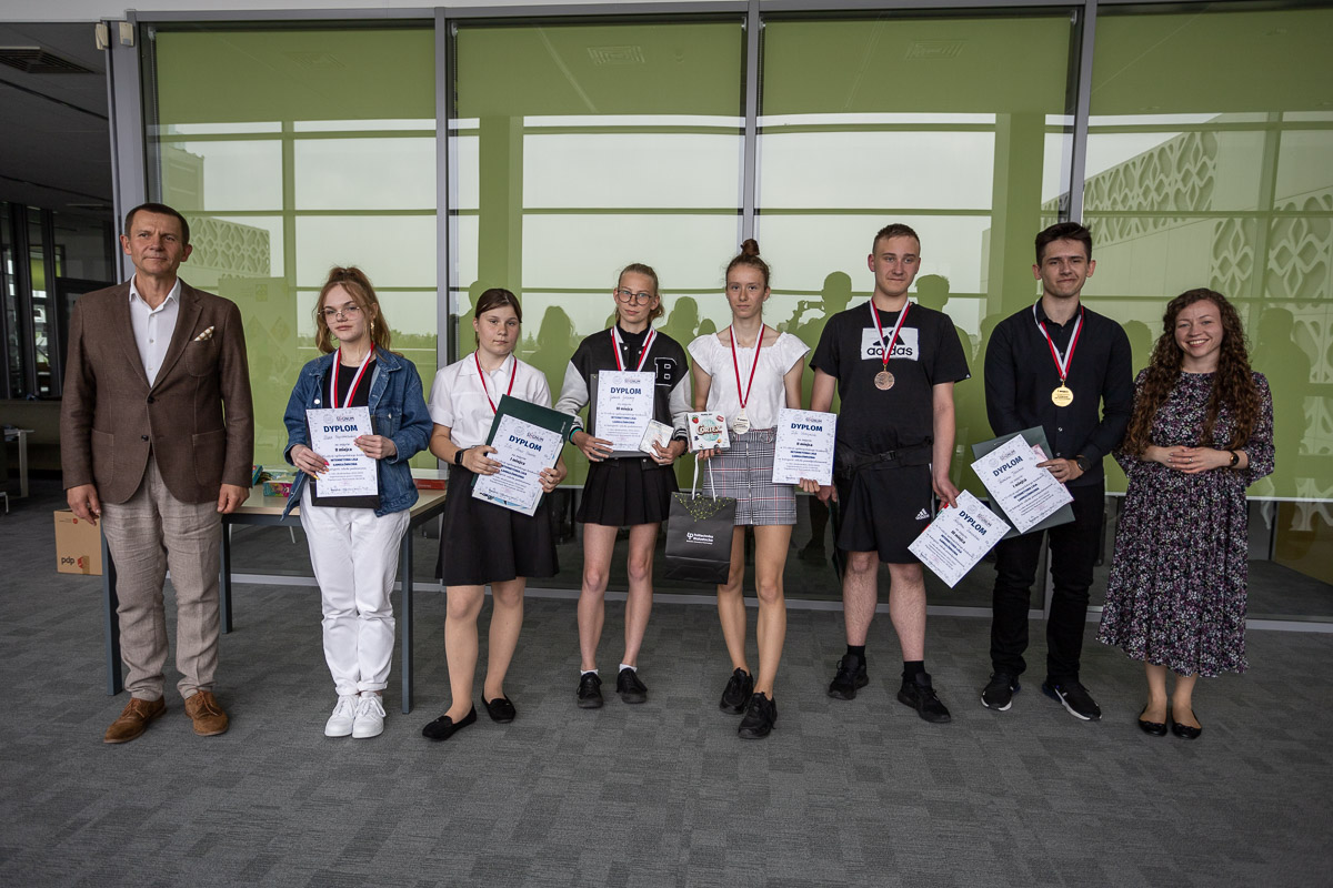 Grupa nagrodzonych uczniów stoi z dyplomami i medalami, obok stoi mężczyzna