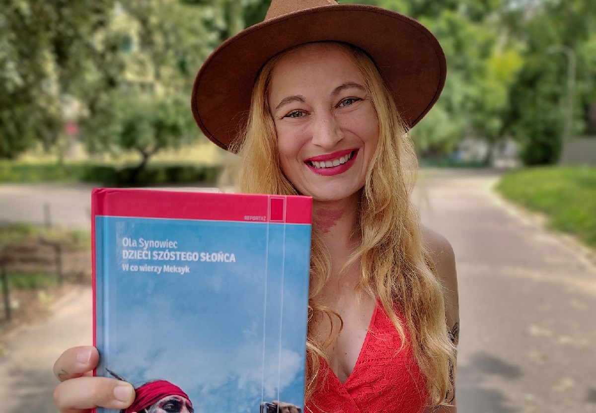 Uśmiechnięta kobieta w kapeluszu trzyma w ręce książkę