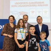 Kobieta, dwóch mężczyzn, uczennica i dwóch uczniów stoją na tle baneru Podlaskiego uniwersytetu dziecięcego
