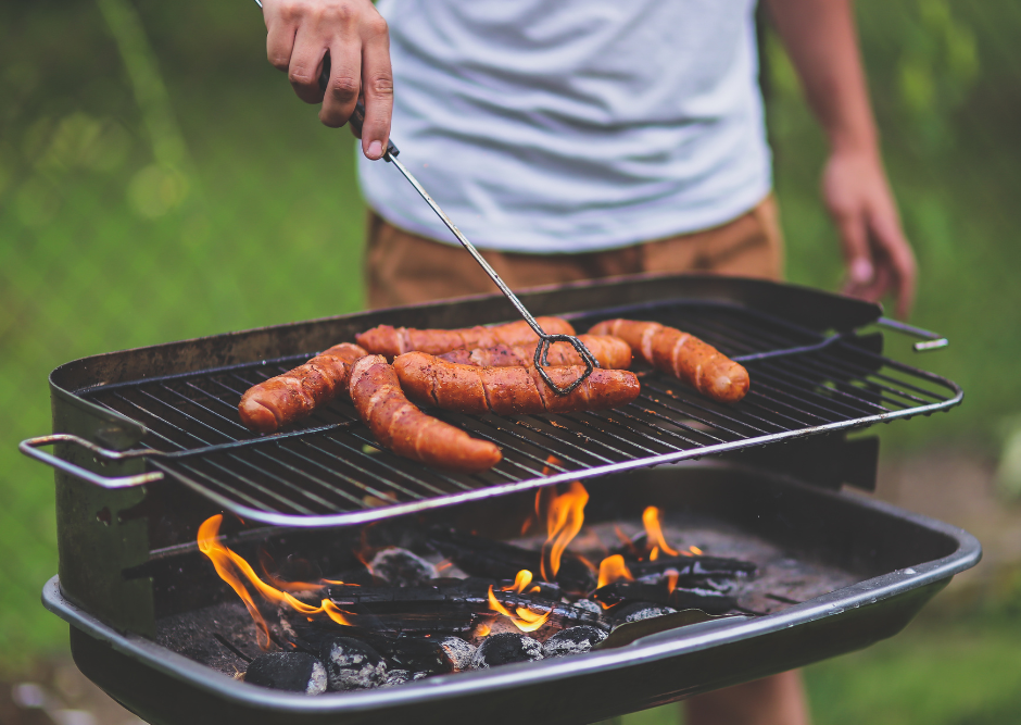 Mężczyzna przekłada kiełbaski na grillu