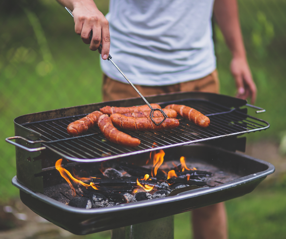 Mężczyzna przekłada kiełbaski na grillu