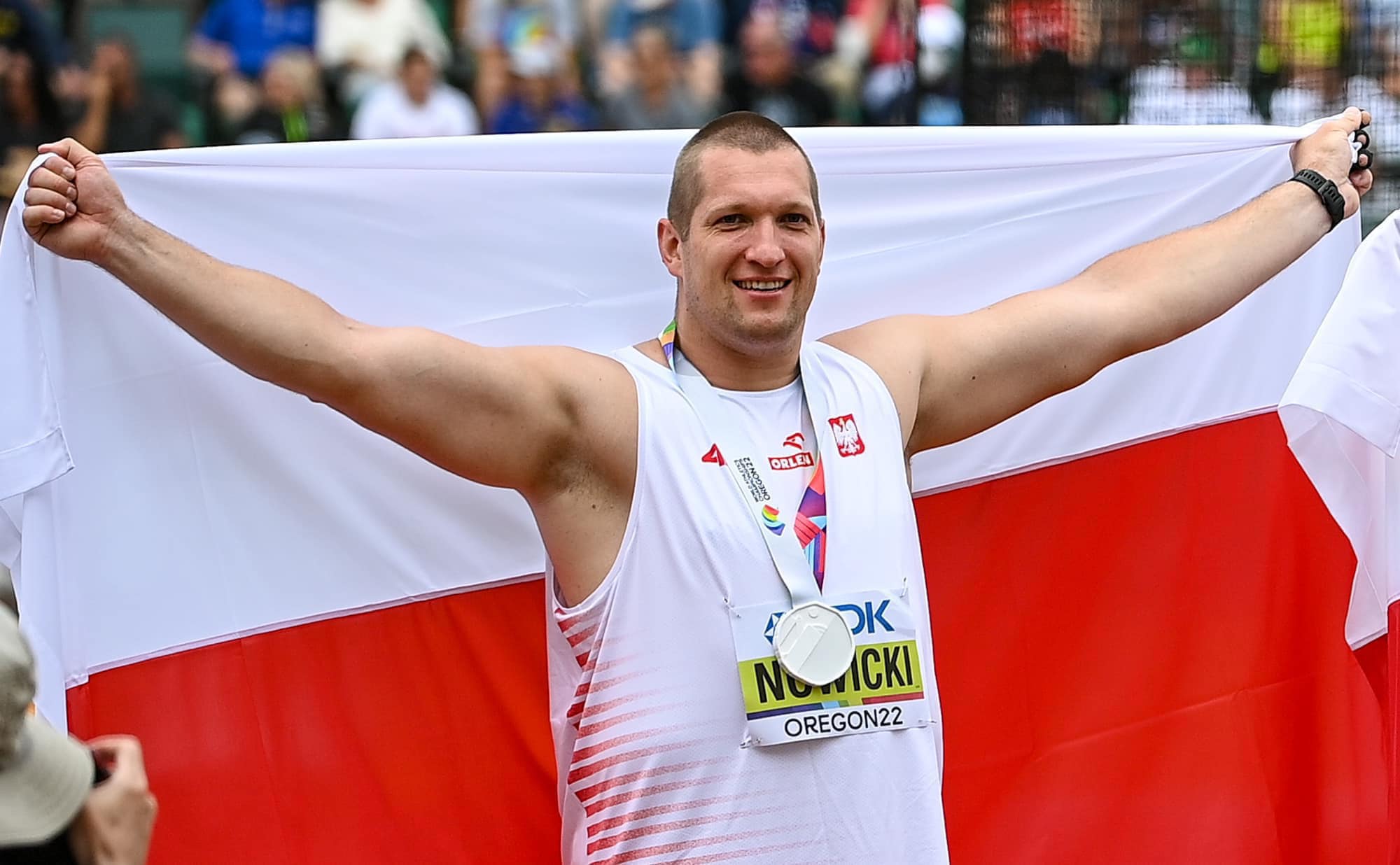 Mężczyzna z medal na piersi trzyma biało-czerwoną flagę