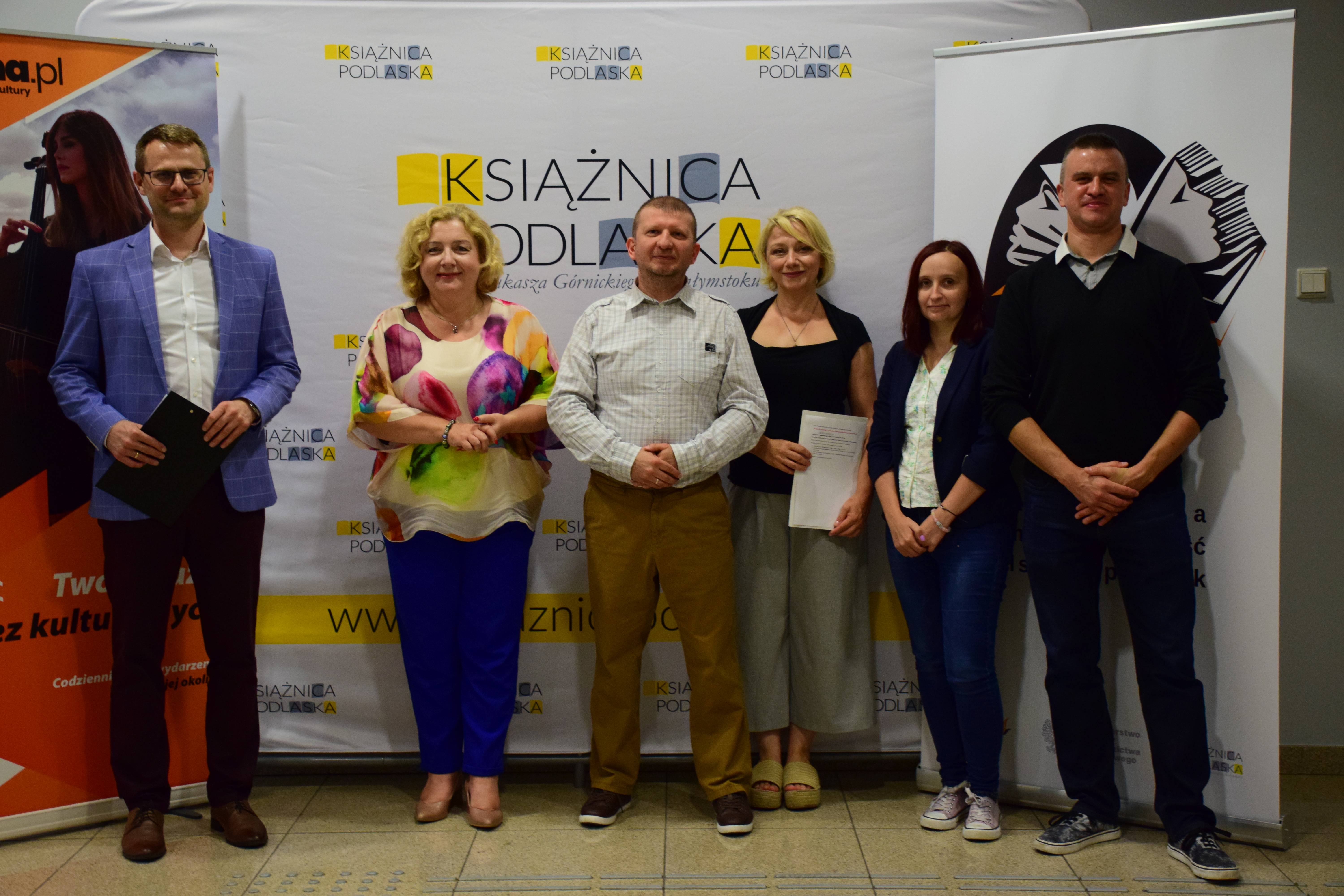 Kilka osób stoi na tle banerów promujących kampanię